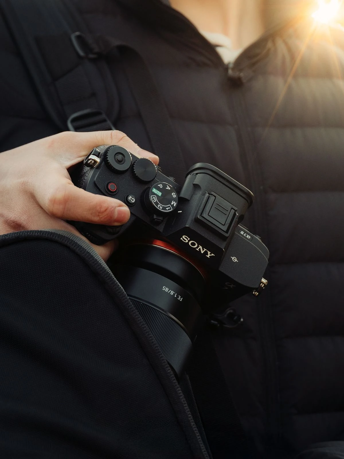 Fotógrafo sosteniendo una cámara Sony junto a su mochila, luz de atardecer de fondo