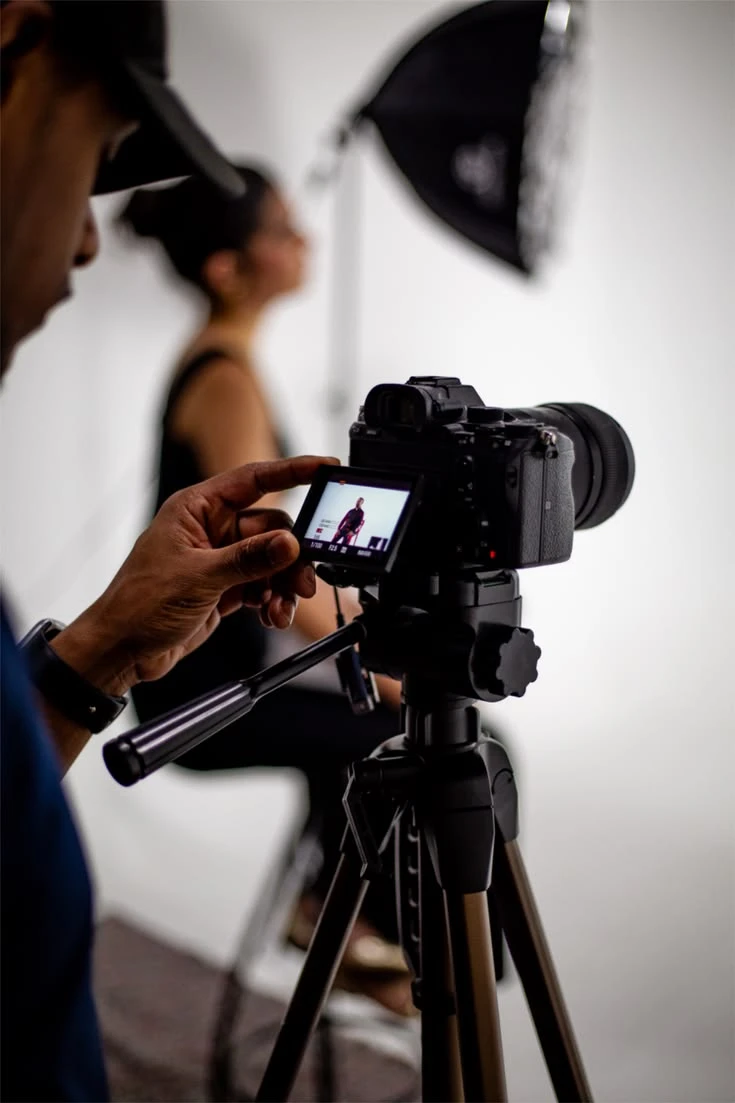 Fotógrafo revisando una toma en cámara, modelo sentada de fondo con softbox